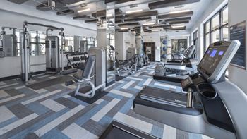 A gym with treadmills and other exercise equipment in a building with windows